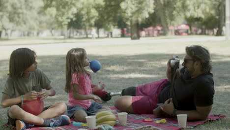 Dad-taking-photo-of-kids-inflating-balloons-at-picnic